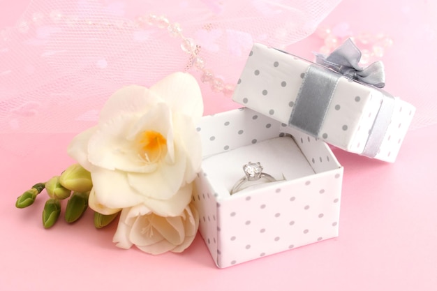 Schöne Schachtel mit Ehering und Blume auf rosa Hintergrund