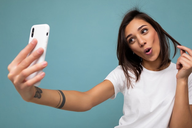 schöne schockierte überraschte junge brünette Frau, die ein lässiges weißes T-Shirt trägt