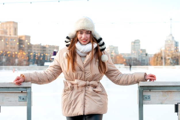 Schöne, schöne junge erwachsene Frau mit brünetten Haaren, warmen Winterjacken, steht in der Nähe der Eislaufbahn im Hintergrund Weihnachtsstimmung auf dem Marktplatz