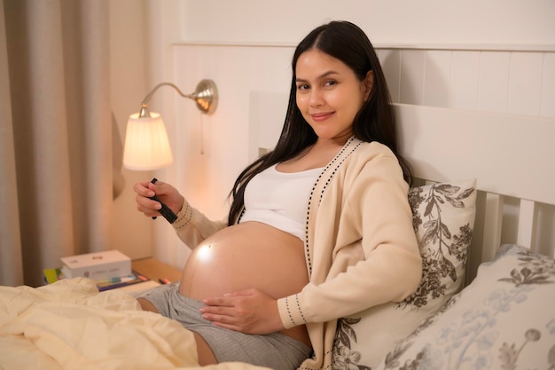 Schöne schwangere Frau benutzt eine Taschenlampe auf dem Bauch, um die Entwicklung eines Babys zu stimulieren