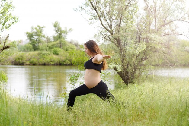 Schöne schwangere Frau, die draußen pränatales Yoga auf Natur tut.