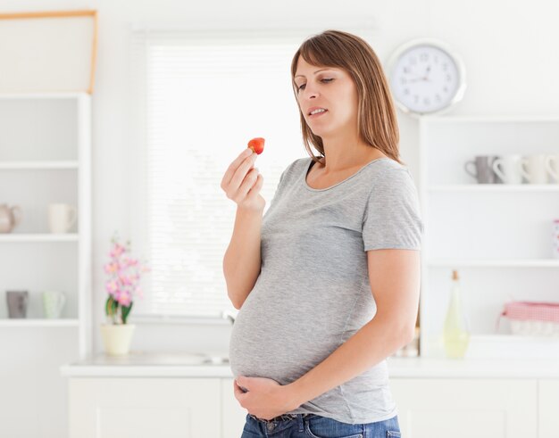 Schöne schwangere Frau, die eine Erdbeere bei der Stellung isst