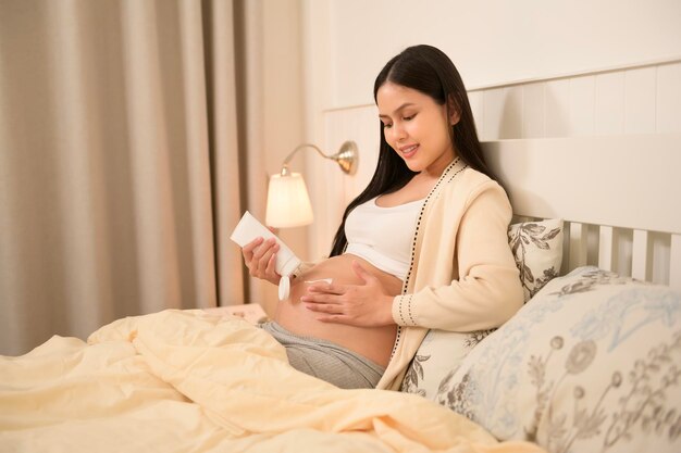 Schöne schwangere Frau, die Feuchtigkeitscreme für Dehnungsspuren auf den Bauch aufträgt