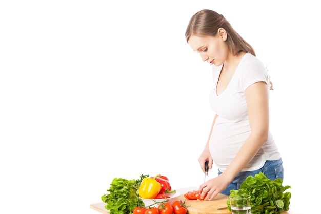 Schöne schwangere Frau, die Gemüse für Salat schneidet. Studioaufnahme