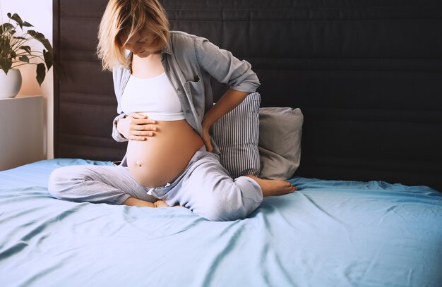 schöne schwangere frau hält hände auf ihrem bauch und liegt zuhause im bett