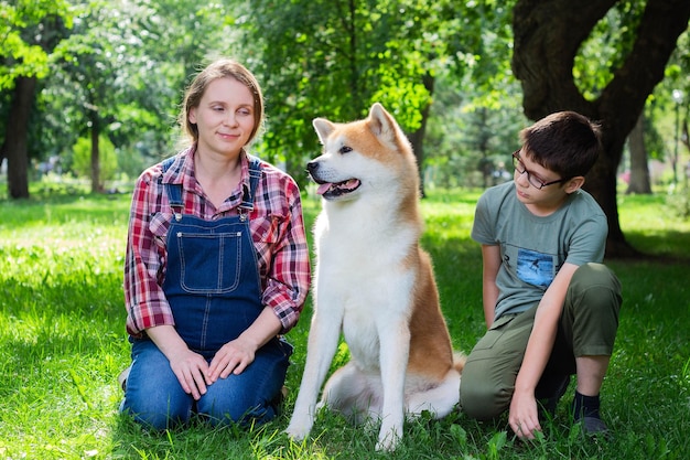 Schöne schwangere Frau in blauen Denim-Overalls mit ihrem Sohn und dem japanischen Hund Akita inu im Park
