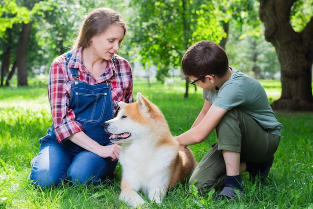 Schöne schwangere Frau in blauen Denim-Overalls mit ihrem Sohn und dem japanischen Hund Akita inu im Park