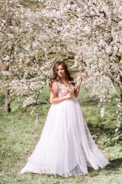 Schöne schwangere Frau in einem langen hellen Kleid geht in einem blühenden Frühlingsgarten.
