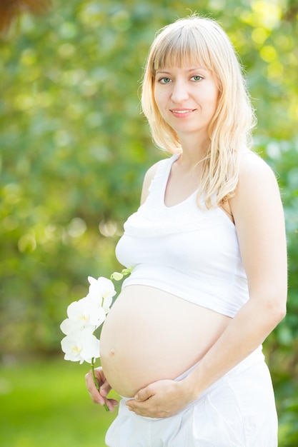 Foto schöne schwangere frau mit blume gegen grünen frühlingshintergrund