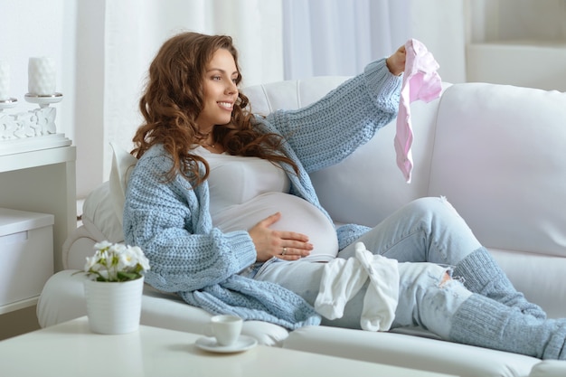 Schöne schwangere Frau mit langen dunklen Haaren mit Babykleidung