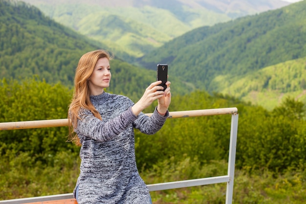 Schöne schwangere Frau mit langen Haaren macht ein Foto auf ihrem schwarzen Telefon friedlicher Natur