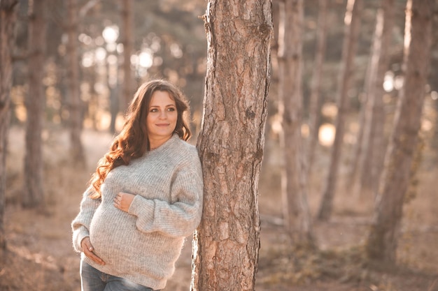 Schöne schwangere Frau trägt eine Strickjacke, die im Freien im Wald posiert