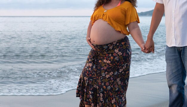 Schöne schwangere Frau und ihr Mann gehen bei Sonnenuntergang am Strand spazieren