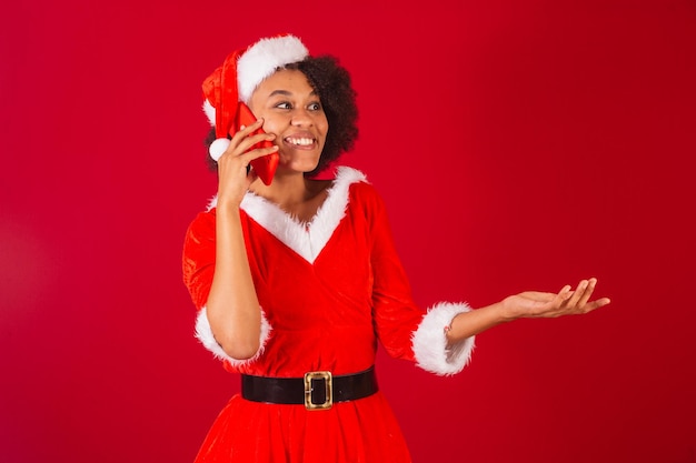 Schöne schwarze Brasilianerin, die als Weihnachtsmann-Mama-Claus verkleidet ist und über Sprachanruf per Smartphone spricht