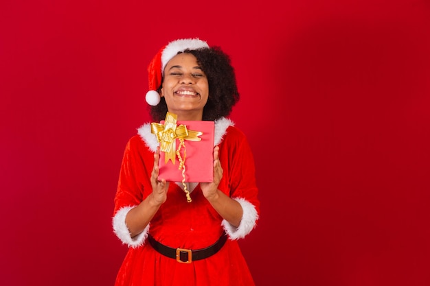 Schöne schwarze Brasilianerin, die als Weihnachtsmann verkleidet ist Mama Claus, die das Geschenk sehr glücklich hält