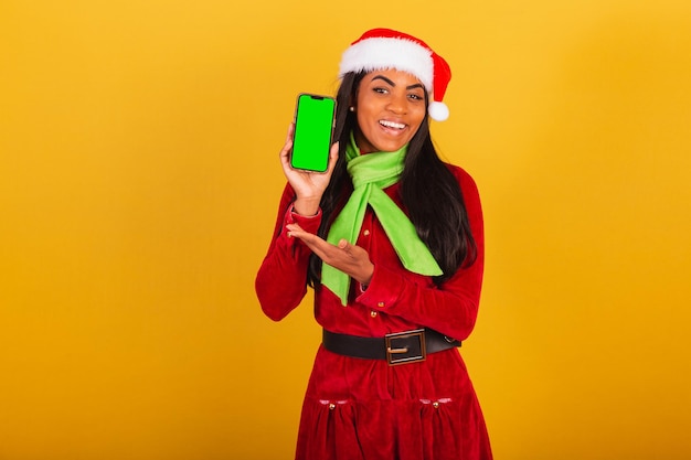 Schöne schwarze Brasilianerin, gekleidet in Weihnachtskleidung, Weihnachtsmann-Smartphone und mit grünem Chroma-Bildschirm