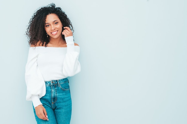 Schöne schwarze Frau mit Afrolockenfrisur. Lächelndes Modell in Pullover und trendiger Jeanskleidung