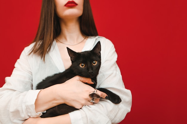 Schöne schwarze Katze in den Händen eines Mädchens in einem weißen Hemd steht