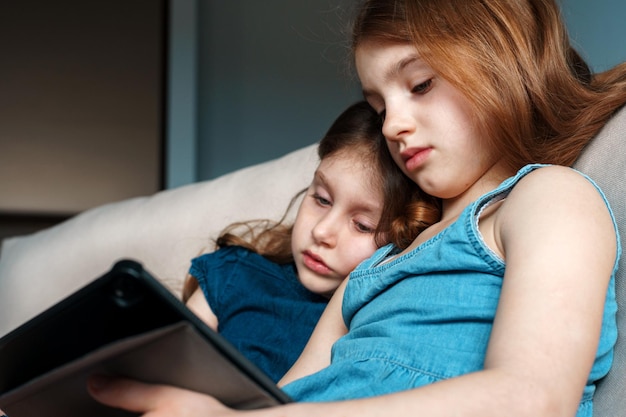 Schöne Schwestern sehen sich zu Hause im Bett ein Video über ein digitales Tablet an
