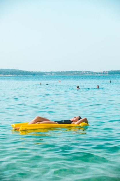 Schöne sexy Frau, die auf gelbe aufblasbare Matratze am Meerwasser Sonnenbaden legt