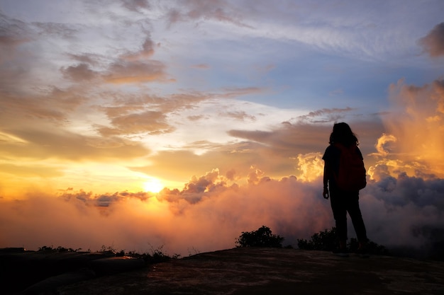 Schöne Silhouette einer asiatischen Frau mit Ziel und Paradies von goldenem Sonnenaufgang und Sonnenuntergang, der im Dschungel auf dem Talberg zu Nebel und Nebel scheint. Erfolgreiches und Lebenshoffnungskonzept