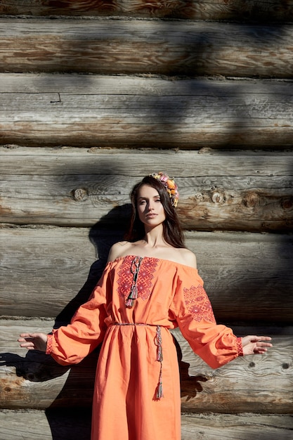 Schöne slawische Frau in einem orangefarbenen ethnischen Kleid und einem Blumenkranz auf ihrem Kopf