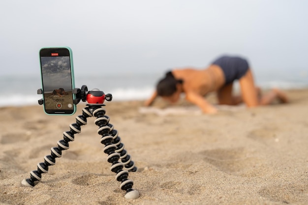 Foto schöne sport-bloggerin trainiert auf dem sand und macht fotos von sich auf einem mobi