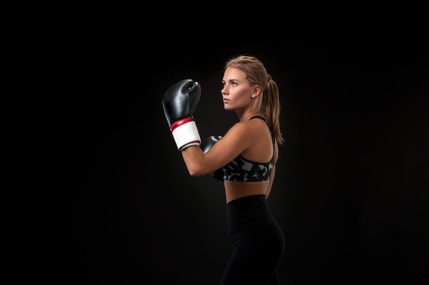 Schöne Sportlerin in Boxhandschuhen, im Studio auf schwarzem Hintergrund. Der Boxer erfüllt den Schlag