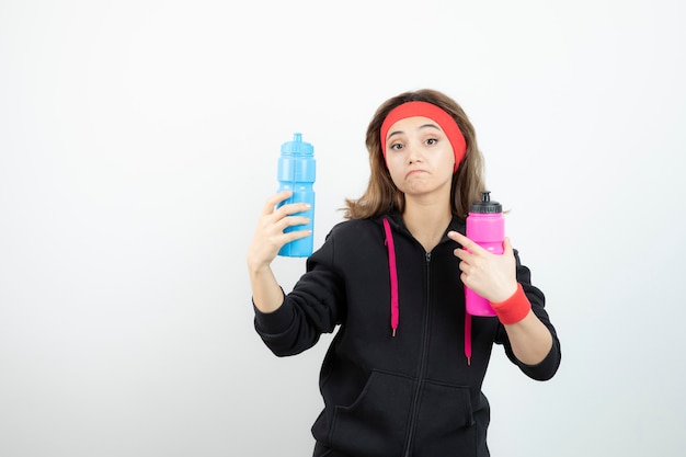 Schöne sportliche Frau, die Flaschen mit Wasser auf weißer Wand hält.