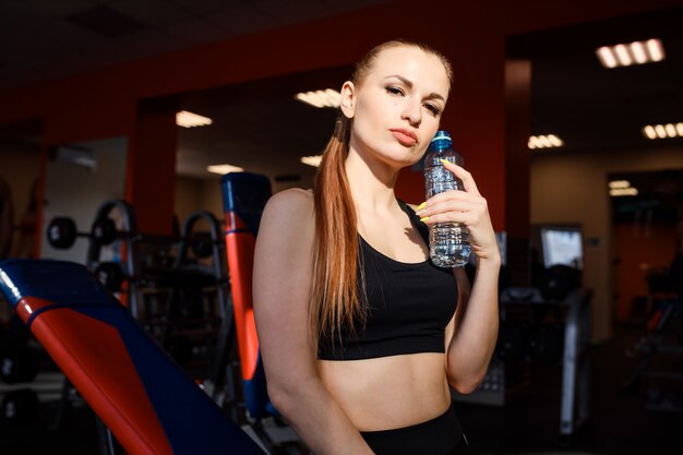 Schöne sportliche Frau im Fitnessstudio hält eine Flasche Wasser.