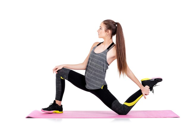 schöne sportliche Frau in Sportkleidung macht Übungen auf Fitness-Matte isoliert auf weißem Hintergrund. dehnen