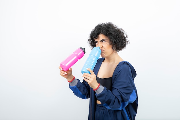 Schöne sportliche Frau mit rosa und blauen Wasserflaschen stehend.