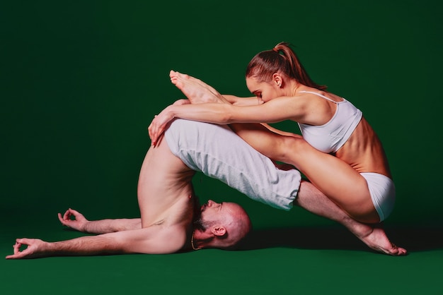 Schöne sportliche Frau und Mann in weißer Kleidung, die zusammen Indoor-Yoga-Asanas machen