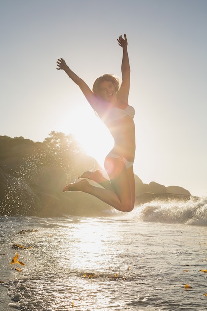 Schöne springende blondine im weißen bikini am strand