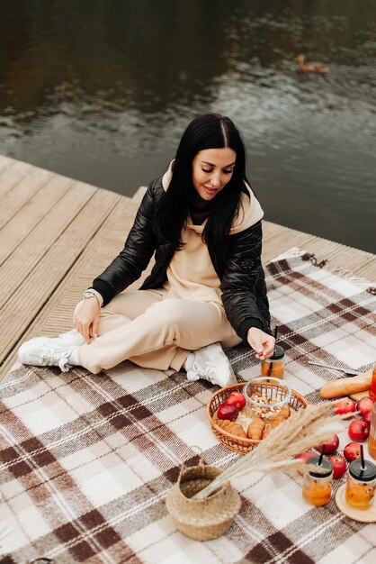 Schöne stilvolle Brünette in einer Lederjacke sitzt auf einem gestreiften karierten Herbstpicknick
