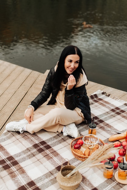 Schöne stilvolle Brünette in einer Lederjacke sitzt auf einem gestreiften karierten Herbstpicknick