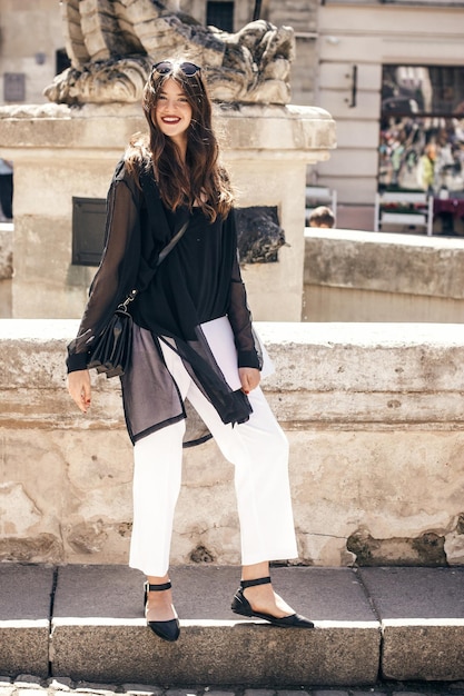 Schöne stilvolle Frau, die in der sonnigen Stadtstraße steht und ein glückliches Hipster-Mädchen der Zeitschrift in modischem Outfit hält, das sich entspannt und den Tag in der europäischen Stadt xA genießt