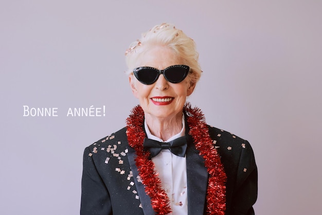 Schöne, stilvolle, reife Seniorin mit Sonnenbrille und Smoking, die das neue Jahr feiert. Lustige Party