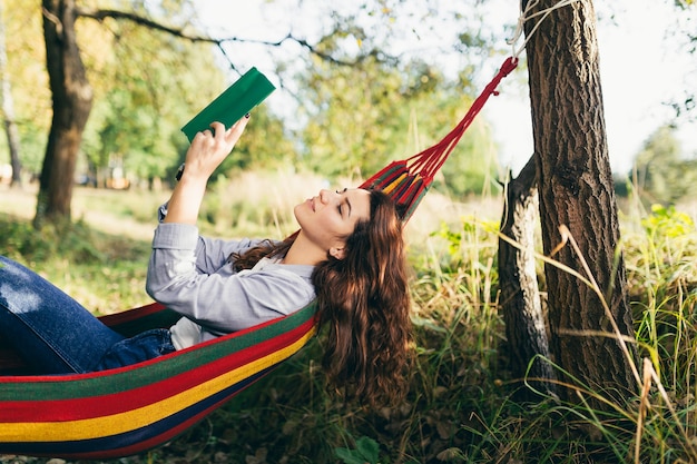 Schöne Studentin, die im Park liegt, der in einer Hängematte liegt und ein Buch liest