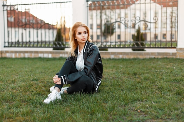 Schöne Studentin in einer stilvollen Jacke und schwarzen Jeans mit weißen Turnschuhen in einer Collage auf Gras