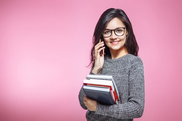 Schöne Studentin mit Büchern sprechend am Telefon auf rosa Hintergrund