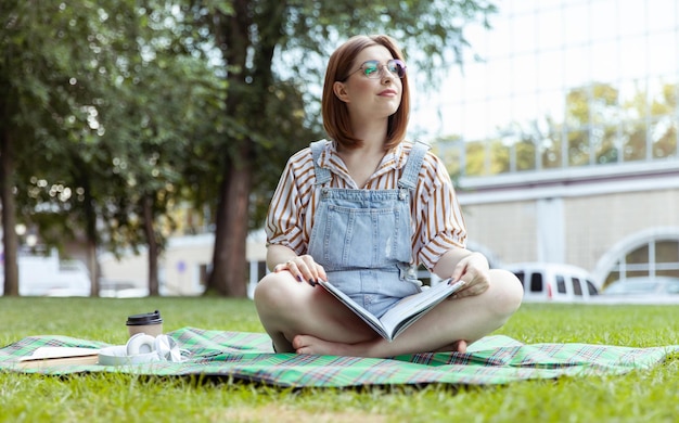 Foto schöne studentin mit einem magazin für hausroboter sitzt im park auf einer decke