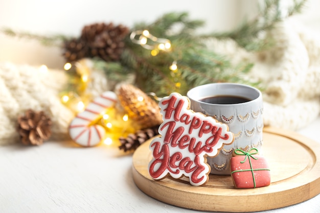 Schöne Tasse mit handgemachten Lebkuchenplätzchen bedeckt mit Glasur nah oben auf einem gemütlichen unscharfen Hintergrund mit Lichtern.