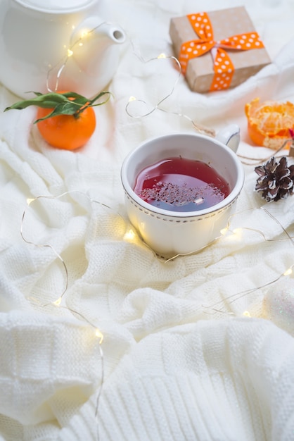 Schöne Tasse Tee mit Mandarinen auf gestrickter weißer warmer Decke