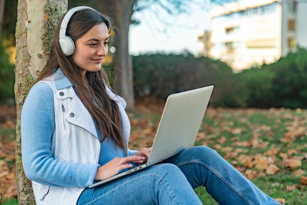 Schöne Teenager-Mädchen sitzen neben einem Baum mit ihrem Computer in einem Park