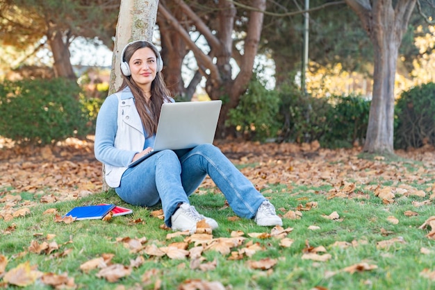 Schöne Teenager-Mädchen sitzen neben einem Baum mit ihrem Computer in einem Park