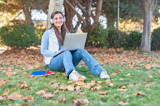 Schöne Teenager-Mädchen sitzen neben einem Baum mit ihrem Computer in einem Park