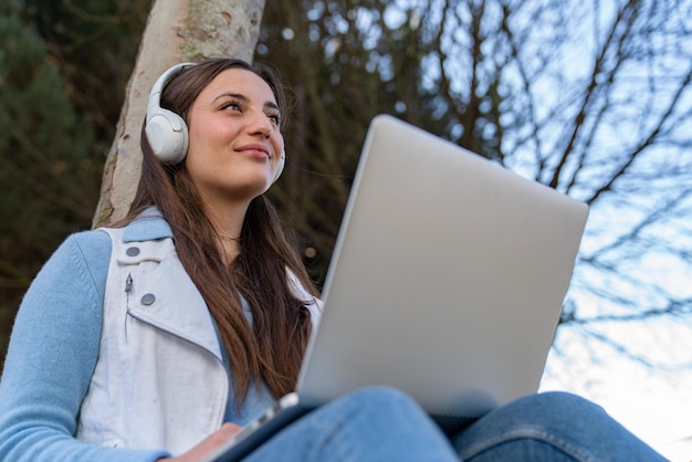 Schöne Teenager-Mädchen sitzen neben einem Baum mit ihrem Computer in einem Park