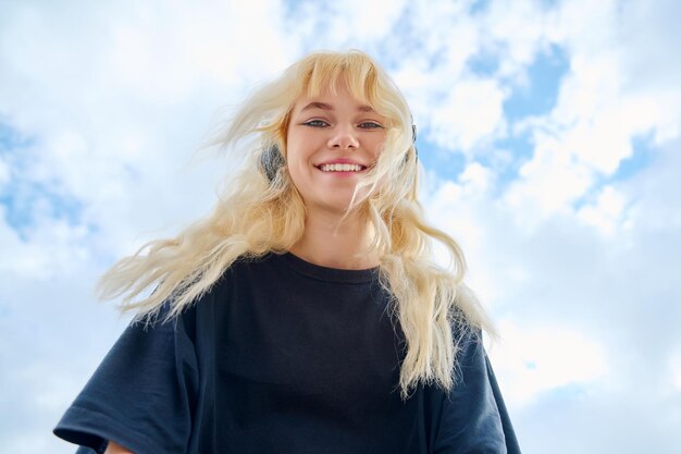 Schöne Teenagerfrau, die blauen Himmel im Wolkenhintergrund hinunterschaut