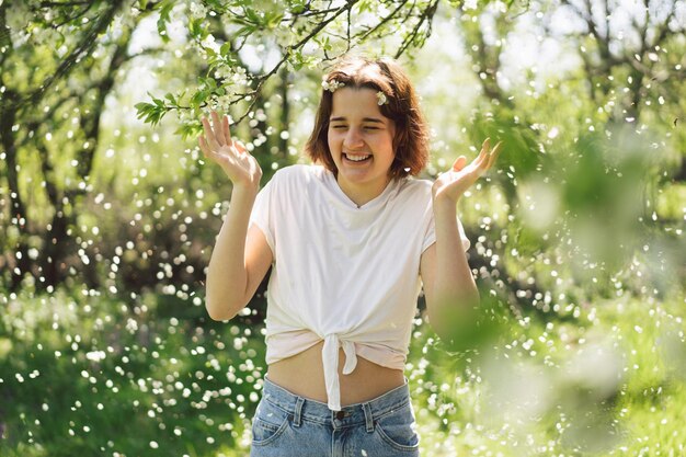 Schöne Teenagerin mit Frühlingsblumen, die die Natur genießt und im Frühlingsgarten lacht